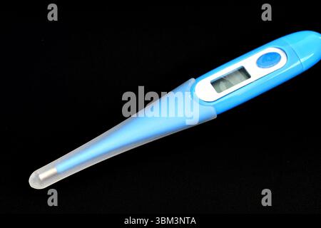 An electronic thermometer for measuring human temperature lies on a black background. Stock Photo