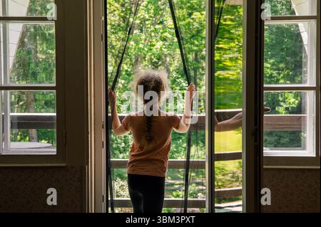 Magnetic mosquito net mesh on balcony door. Child going outdoors to home balcony through, preventing insects coming inside. Stock Photo