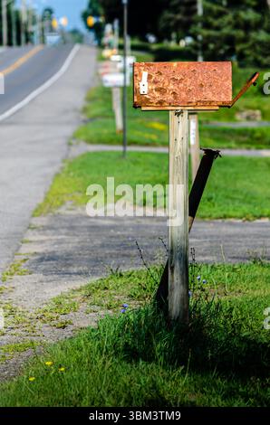 Rusty rural mailbox in front of a row of out of focus mail boxes next to a road in the summer. Stock Photo