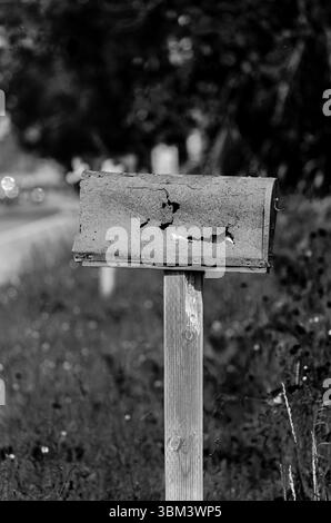 Monochrome rusty, damaged rural mailbox  in front of trees in the summer. Stock Photo