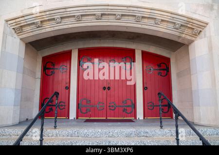 A bold pair of red double doors set in a textured beige wall, casting dramatic shadows under warm afternoon light, symmetry and vintage charm for arch Stock Photo