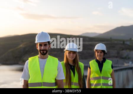 Engineers wearing safety vests and helmets working at sunset near a dam Stock Photo