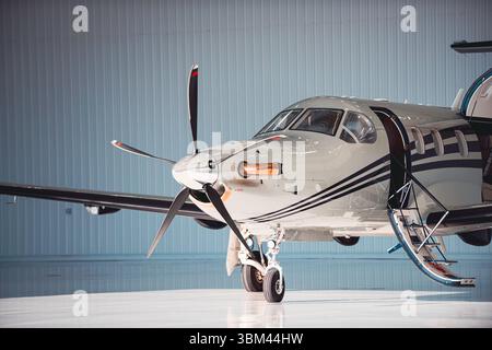Side-front view of a turboprop aircraft parked inside a hangar with the cabin door open and stairs extended, captured in warm directional light. Stock Photo