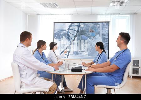 Team of doctors using video projector during conference about DNA indoors. Illustrations on projection screen Stock Photo