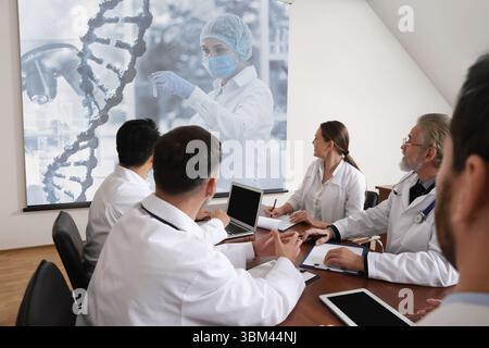 Team of doctors using video projector during conference about DNA indoors. Illustrations on projection screen Stock Photo