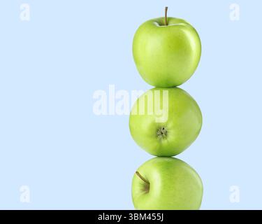 Green apples stacked on top of each other against light blue background. Balance Stock Photo