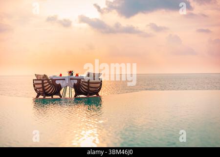 Romantic luxury honeymoon dinner at infinity pool with seascape view, sunset reflections on sea and sky, destination dining experience tropical resort Stock Photo