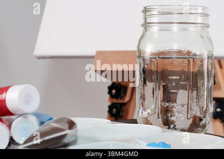 Mason Jar of Water with Canvas and Paint – Artist’s Painting Setup Still Life Stock Photo