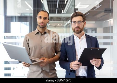 Two diverse business professionals standing confidently in a modern office setting, ready for business. Stock Photo
