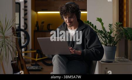 Glad Hispanic guy worker using laptop at home man freelancer typing computer programmer work remote job developer browse web male in headphones Stock Photo