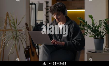 Glad Hispanic guy worker using laptop at home man freelancer typing computer programmer work remote job developer browse web male in headphones Stock Photo