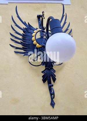 View of a wrought iron lantern in the shape of a stylized dragon with a gilded element on the wall of a building in the Alpine resort town of Ortisei Stock Photo