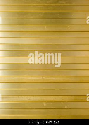 Wall or ceiling covered in horizontal, golden or brass aluminum slats, creating a sleek and modern aesthetic. Stock Photo