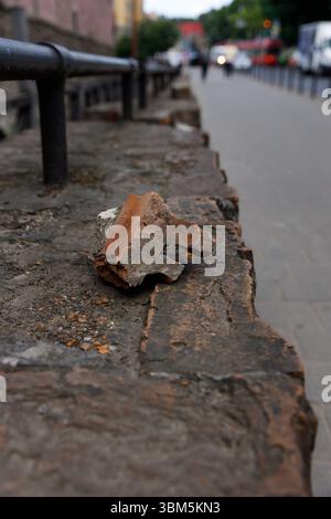 The image features a close-up view of a broken stone piece lying on a weathered stone surface. In the background, a blurred urban setting showcases pe Stock Photo