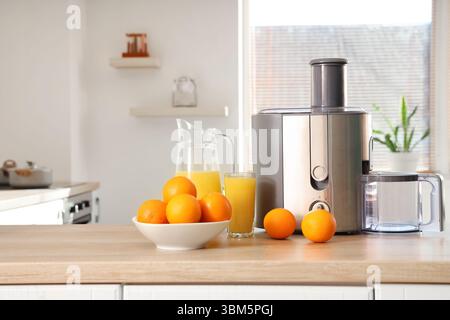 Modern juicer with oranges on table in kitchen Stock Photo