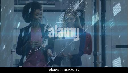 Walking team in blazers carrying laptop, mug past glass partitions at office, with holographic data. Collaboration, innovation, technology, profession Stock Photo