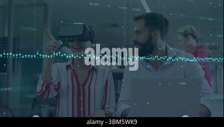 Collaborating tech duo using VR headset and laptop at office, showing holographic overlay. Technology, innovation, digital, futuristic, teamwork, mode Stock Photo