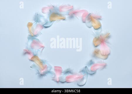 Happy easter greeting card template. Round frame made of colorful feathers on pastel blue background. Flat lay, copy space Stock Photo