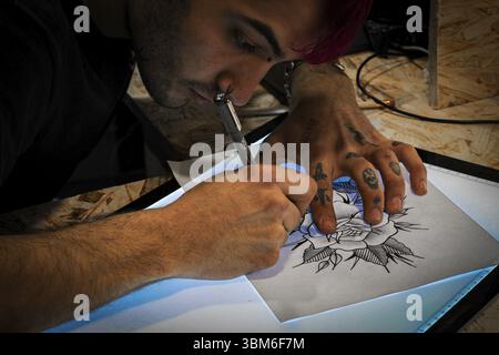 Tattooist designing a tattoo drawing on paper on a digital drawing tablet in his tattoo studio Stock Photo