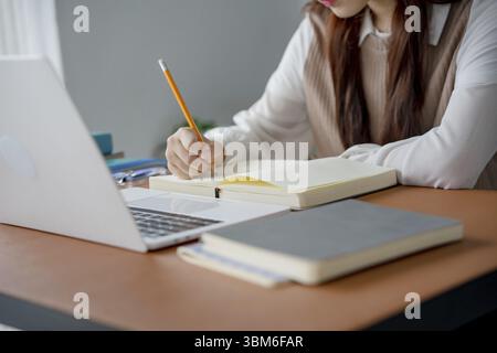 Asian woman using laptop to study student engaged in online learning at college Stock Photo
