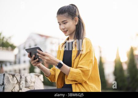 Smiling young Asian woman using digital tablet in urban city Stock Photo