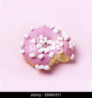 Bitten pink icing donut with marshmallows on pink background. Minimal concept Stock Photo