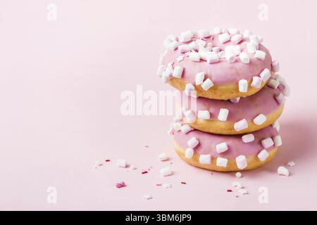 Tower of pink glazed donuts with marshmallows on pink background Stock Photo