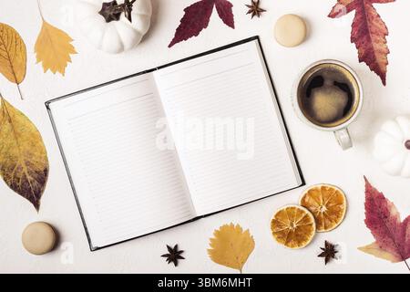 Notepad and cup of coffee on white table with autumn leaves pattern Stock Photo