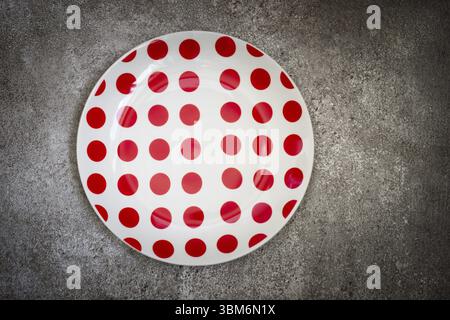 Empty White in red dot ceramic plate On a concrete background. Top view with copy space Stock Photo