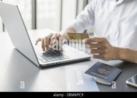 Hand Man Online booking and buying plane tickets using laptop phone and credit card Planning trip travel vacation with passport and ticket Stock Photo