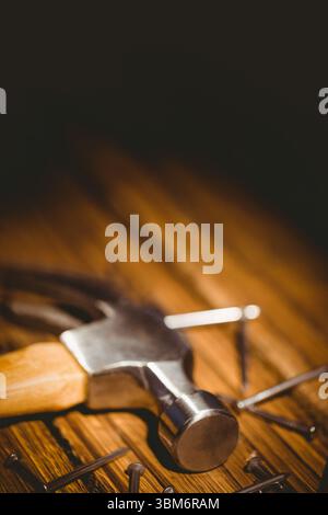Claw hammer is resting on wooden tabletop with scattered nails, 3D render highlighting warm light Stock Photo