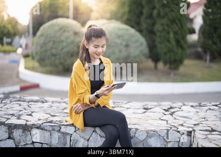 Smiling young Asian woman using smartphone in urban city checking apps mobile outdoors Stock Photo