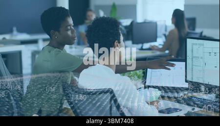 Collaborating two women colleagues reviewing floor plans in modern open-plan office, with monitors. Teamwork, innovation, modernity, productivity, tec Stock Photo