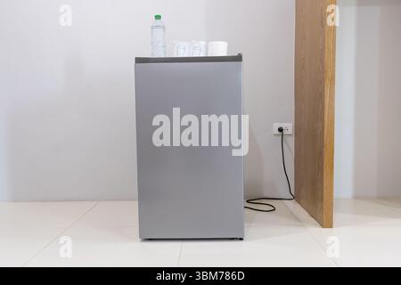 A gray refrigerator or fridge is plugged into the wall socket in hotel or resort room. Stock Photo