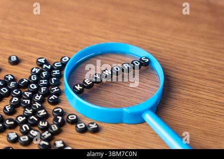 A blue magnifying glass with alphabet beads that spell out KEYWORDS. Searching, optimization, discovery, SEO, data, and online content concept. Stock Photo