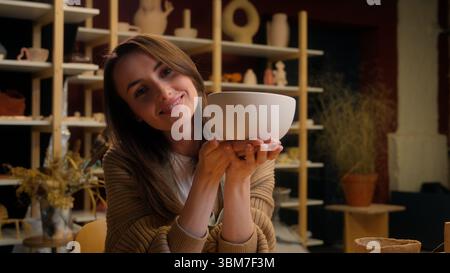 Smiling Caucasian woman girl female artist sculptor artisan potter small business owner saleswoman holding bowl ceramics modeling clay handmade Stock Photo