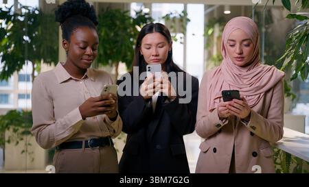 Three diverse multiracial business women addicted mobile phones businesswomen African Asian Muslim girls addiction gadgets in office females using Stock Photo