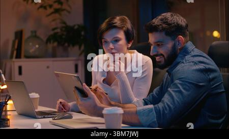 Multiracial teamwork Indian man Caucasian woman business partners co-workers colleagues talking at dark night evening office girl guy businessman Stock Photo