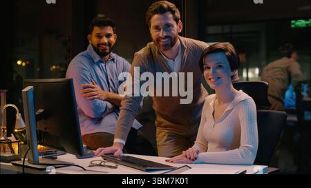 Business colleagues businessmen businesswoman men woman multiracial co-workers talking friendly conversation night evening office work overtime Stock Photo