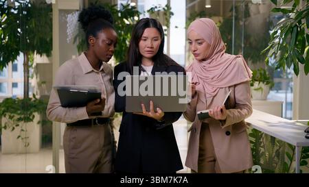 Multiracial business women group in office diverse businesswomen meeting discussion team project laptop African Asian Arabian people team girls talk Stock Photo