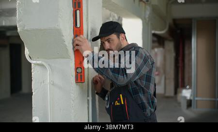Man builder engineer checking wall with bubble level tool building construction electrician inspector foreman repairman guy male industry architect Stock Photo