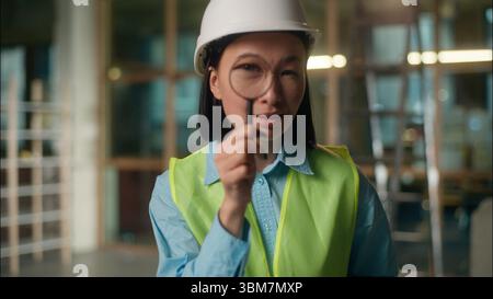 Asian woman builder investigator architect looking through magnifier Chinese Korean Japanese girl civil engineer searcher big zoomed eye vision spy Stock Photo