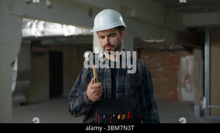 Man builder confused holding hammer tool Caucasian guy male architect engineer foreman on construction site building industry repairman architect Stock Photo