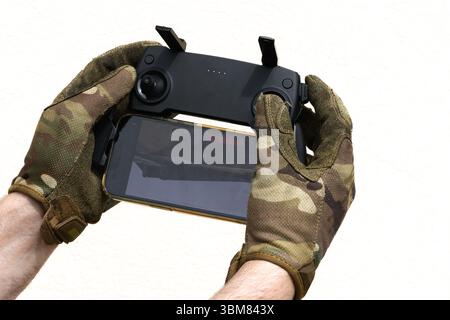 Operator in military colored gloves holding remote control panel Unmanned aerial copter pale background Stock Photo