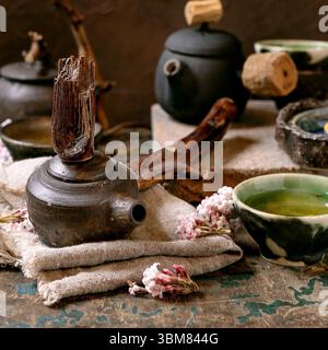 Chinese Tea Ceremony. Three traditional handmade ceramic black teapots with wooden handle on dark wooden table. Ceramic teacups and pink spring flower Stock Photo