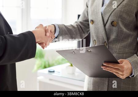 Two businesswomen in formal suits shaking hands in office, establishing partnership and making deal. Stock Photo