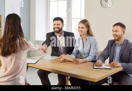 Smiling HR managers sitting at desk and shaking hands with female candidate during job interview. Stock Photo