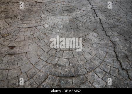 Close-up of cracked concrete pavement with semicircular tile pattern. Aged urban surface, perfect for backgrounds, textures, and construction-related Stock Photo