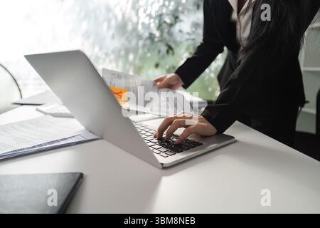 Business analysis. Professional accountant working on a laptop while reviewing financial documents in the office. Stock Photo
