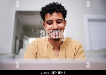 Smiling Man Working From Home With a Positive Attitude While Using a Laptop Stock Photo